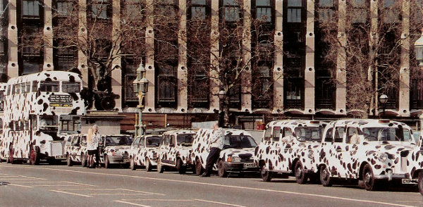 YA1a: Scene from 102 Dalmatians with several spotted vehicles lined up along a London street